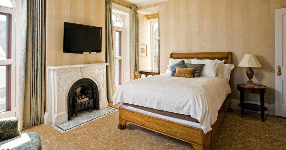 A brightly-lit room with a short bed and a wall-mounted television above a fireplace.
