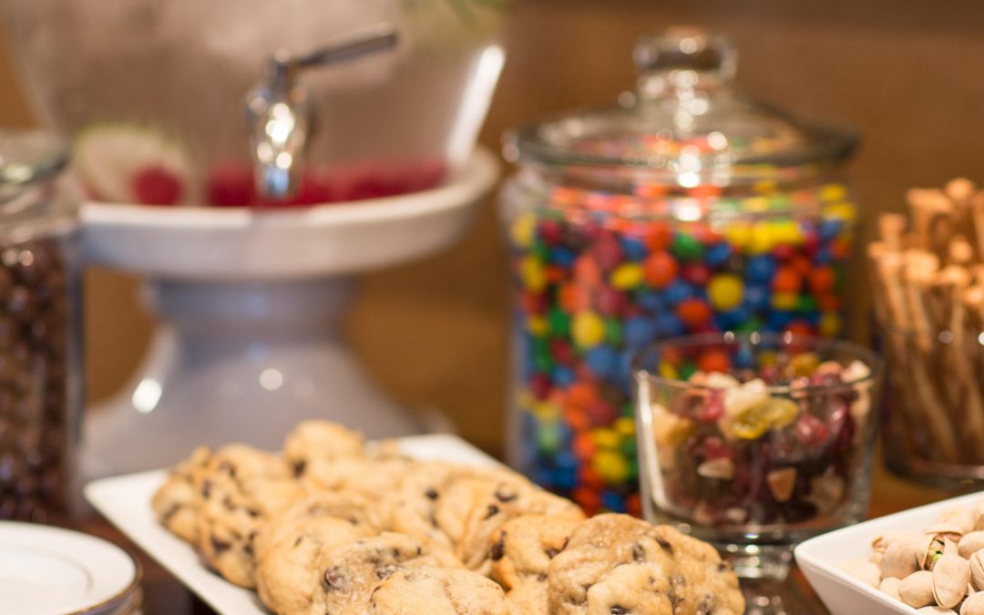 A plate of chocolate chip cookies is next to a jar of colorful chocolate candies.