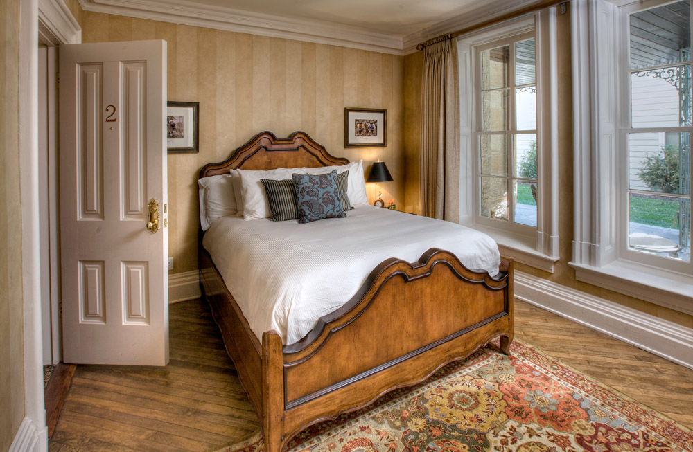 A queen bed looking outside through a pair of floor-to-ceiling windows.