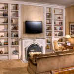 Lounge or library with in-wall bookshelves and a television above a fireplace.