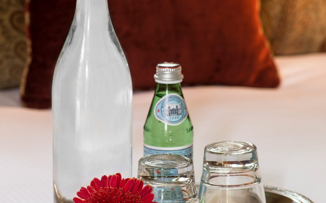 A tall bottle of still water and a small bottle of sparkling water along with two downturned glasses on a tray with a red paper daisy.