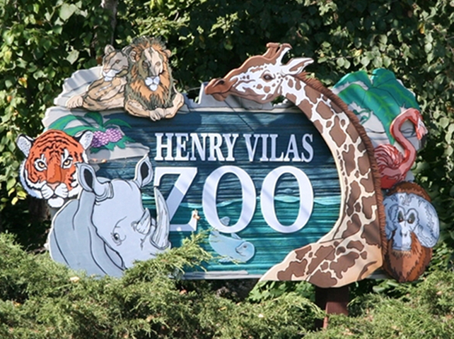 The wood-carved sign at the entrance of the Henry Vilas Zoo, featuring a seal, rhinoceros, tiger, male and female lions, a giraffe, orangutan, and a flamingo.
