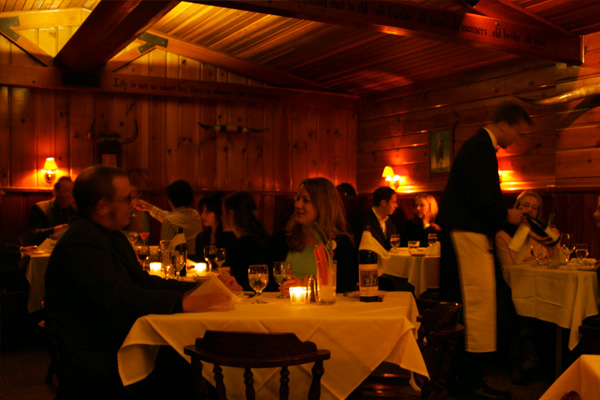 A dimly-lit and cozy, wooden interior of a room full of people appearing to enjoy their dinner.