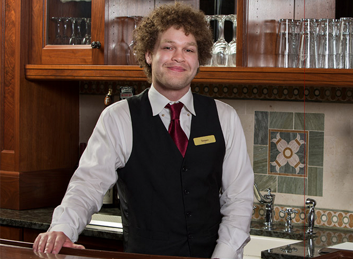 Terrance, with curly hair, standing behind a bar, smiling at the camera.